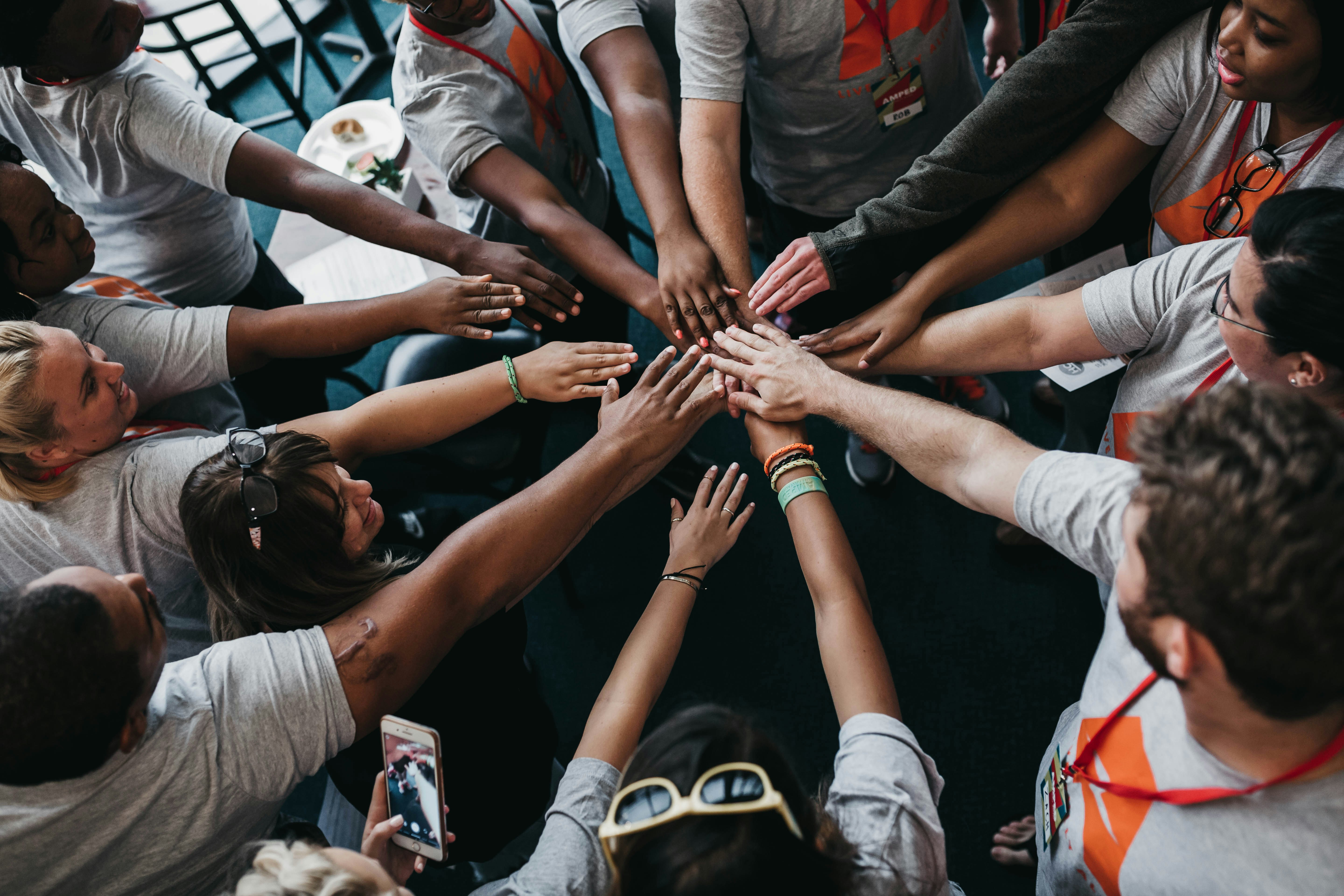 A diverse group of community members raising their hands together in a huddle, symbolizing collective awareness and looking out for one another